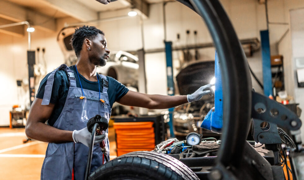 Young mechanic working on car maintenance, inspecting wheel and chassis in a professional auto repair shop