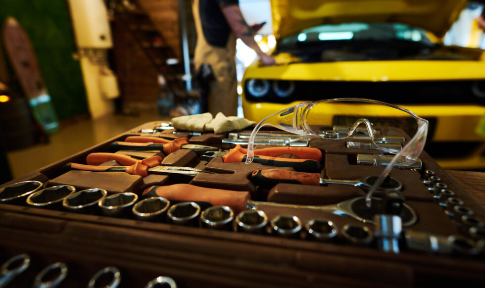 Protective eyeglasses on top of kit with spare parts and handtools for repair and checkup work of cars against repairman